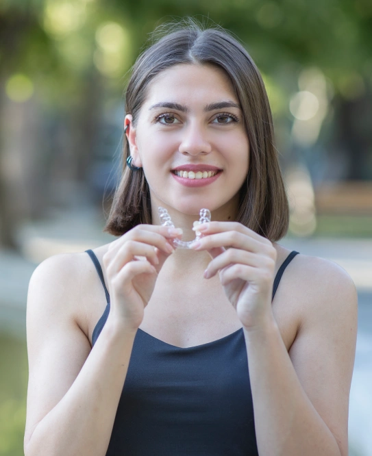 Young woman holding a clear aligner tray and smiling outdoors