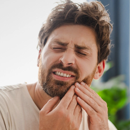 Man grimacing in severe tooth and jaw pain indicating need for emergency dental care