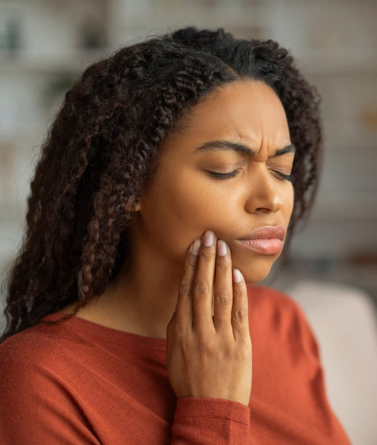 Young woman holding her cheek in pain indicating a dental emergency requiring immediate care